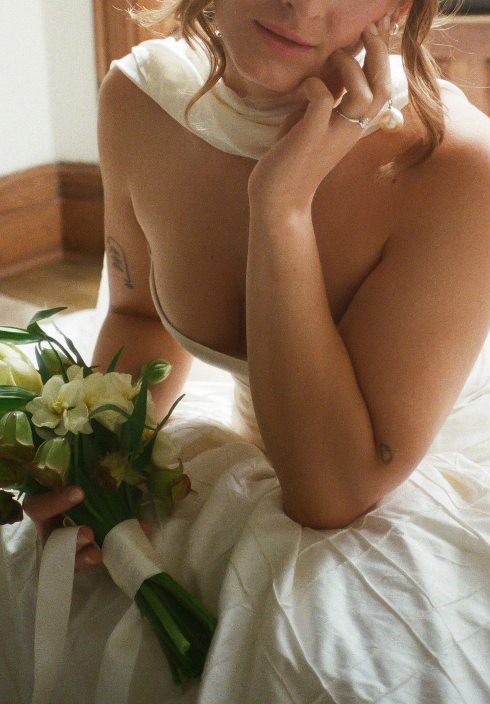A person in a white dress holds a bouquet of white flowers while sitting in soft natural light.