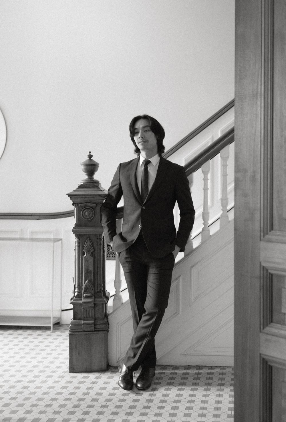 Black and white photo series showing a person in a suit leaning against a wall near an ornate staircase banister.
