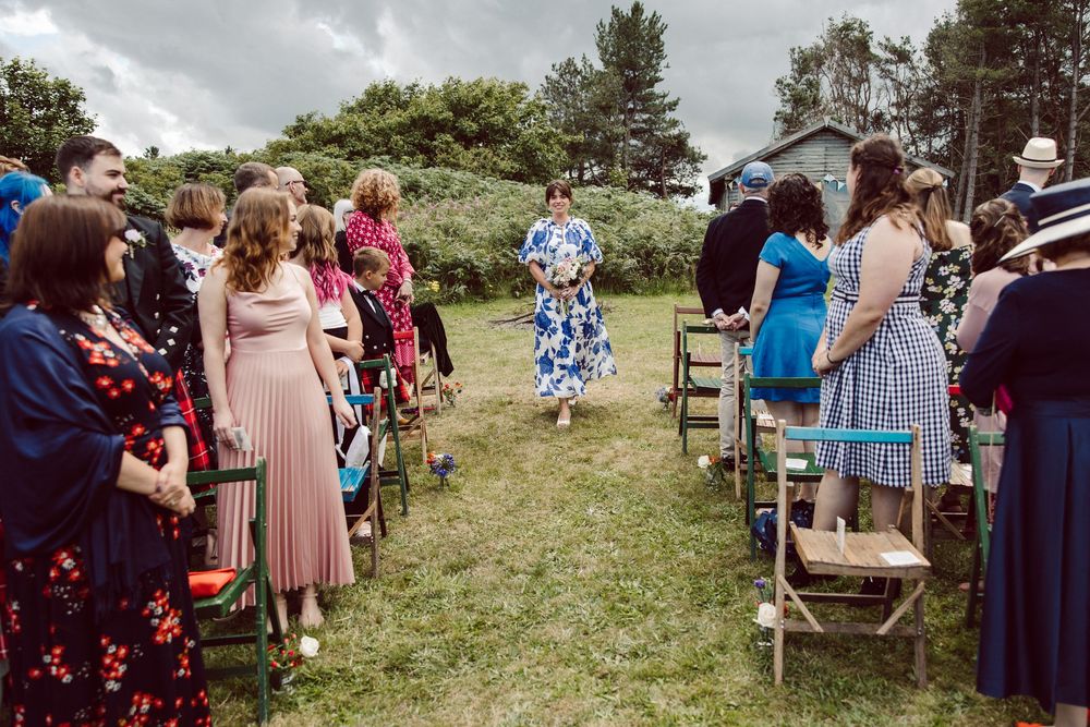 Wedding guests gather outdoors on a grassy hillside for a scenic ceremony celebration.