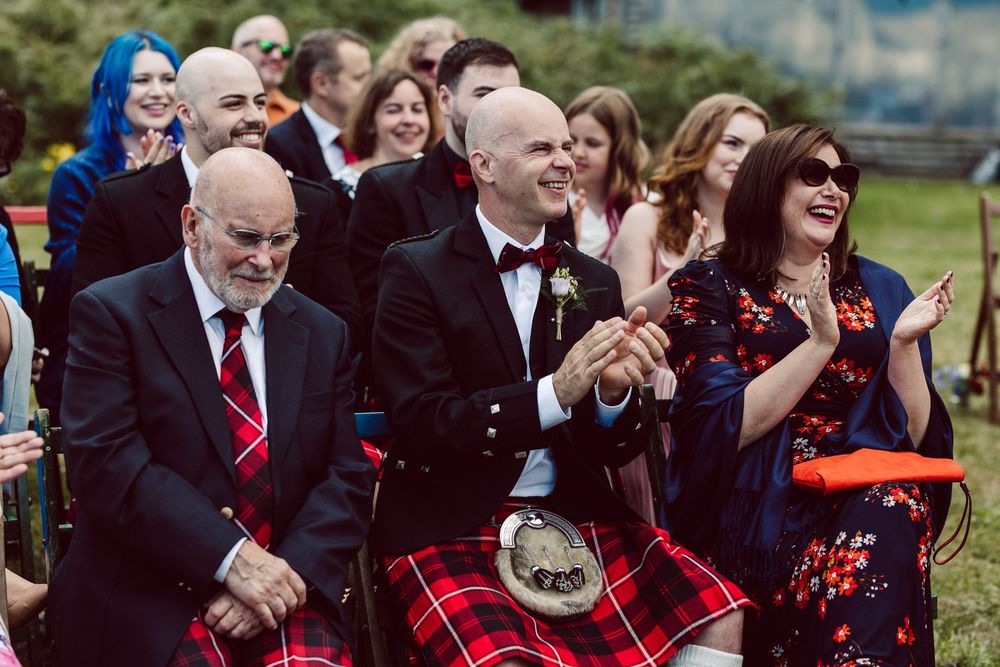 Wedding guests enjoying emotional moments during outdoor ceremony in Scottish Highland attire.