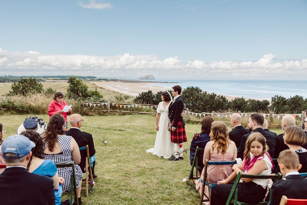 Guests seated in wooden chairs for outdoor wedding ceremony with ocean views and blue sky backdrop.