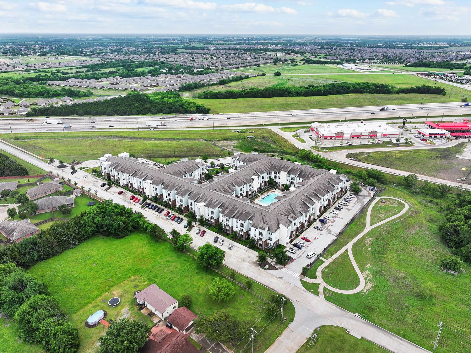 Aerial view of a large residential townhome complex near a highway, surrounded by green fields in a suburban area.