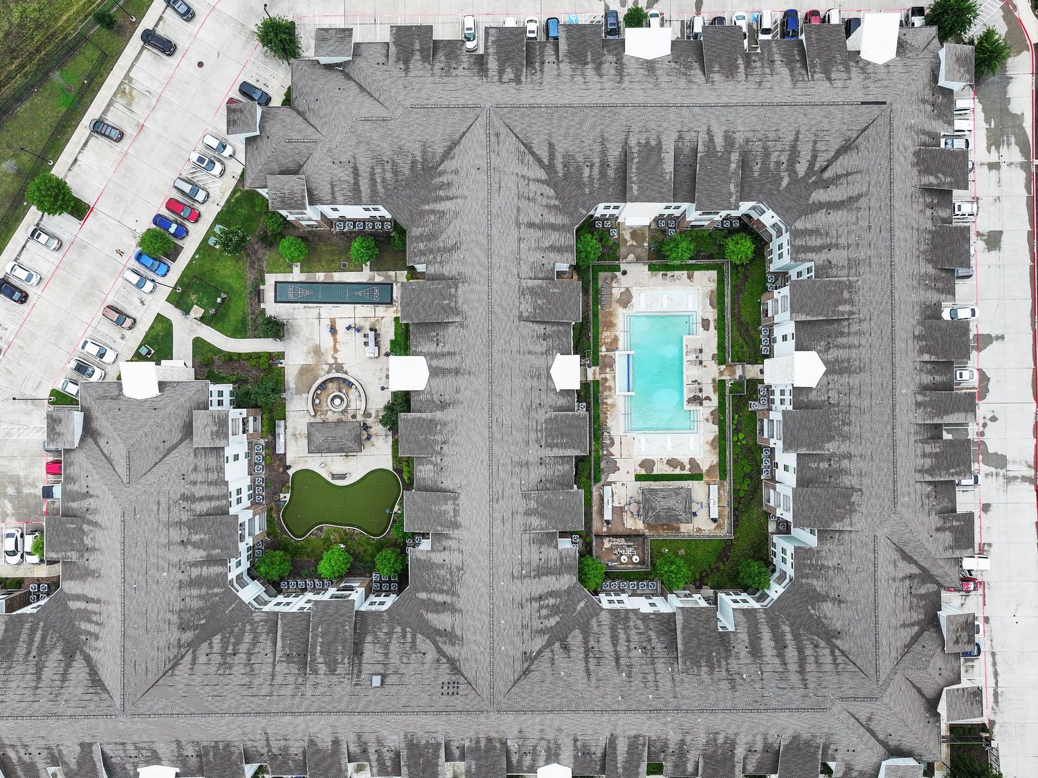 Aerial view of two U-shaped apartment complexes with courtyards featuring a pool and landscaping.