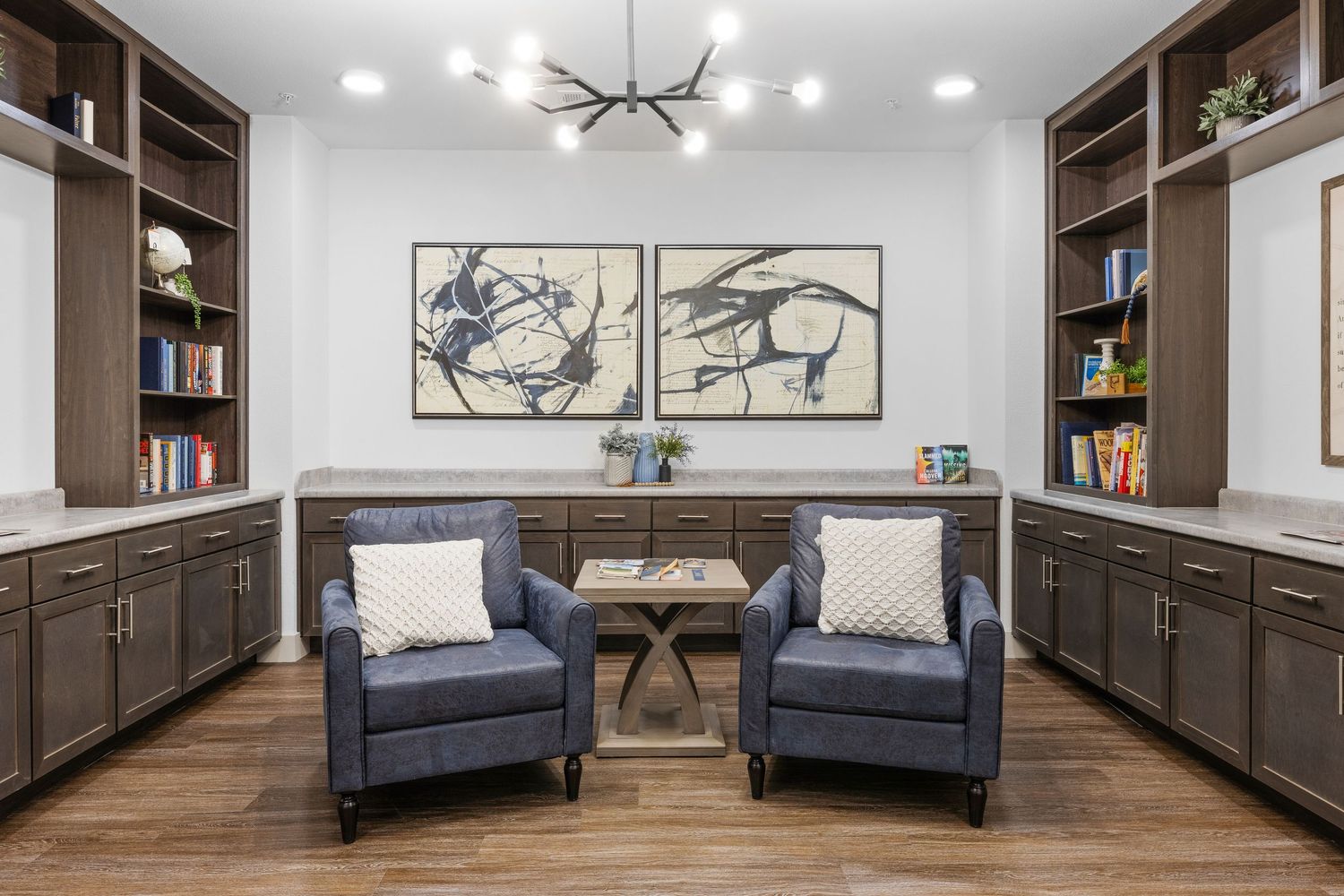 Elegant clubhouse lounge with navy blue armchairs, built-in shelving, and contemporary chandelier.