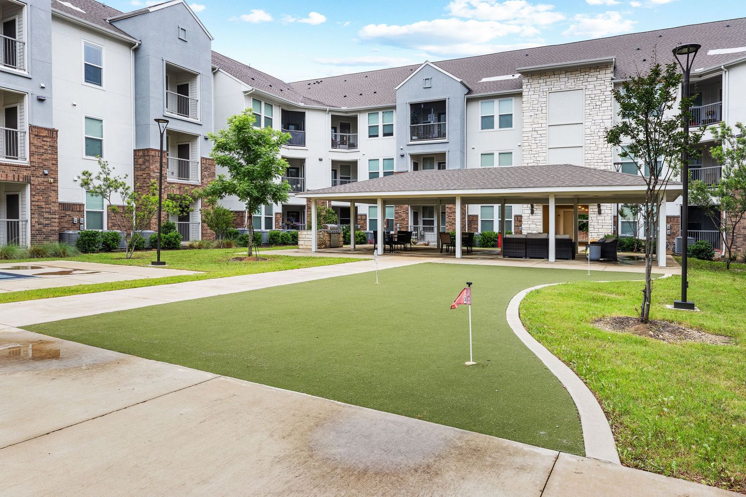 Luxury apartment complex with a putting green, covered patio, and lush landscaping in a courtyard setting.