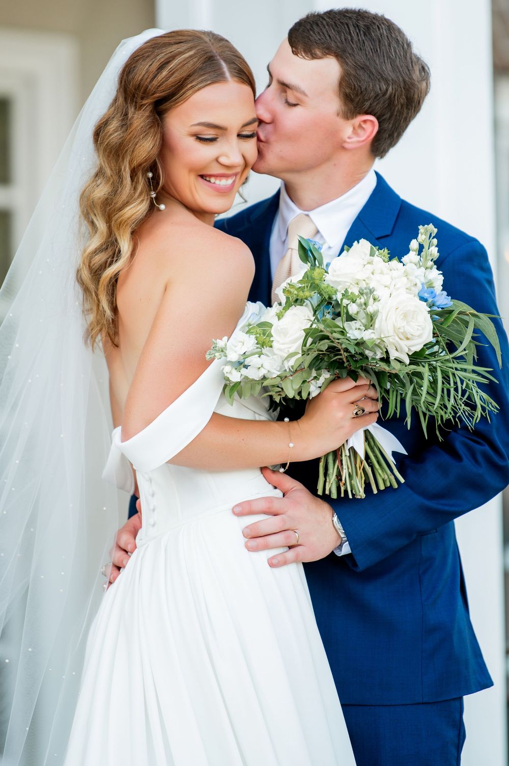 Romantic wedding portraits of couple in navy suit and white gown embracing outdoors.