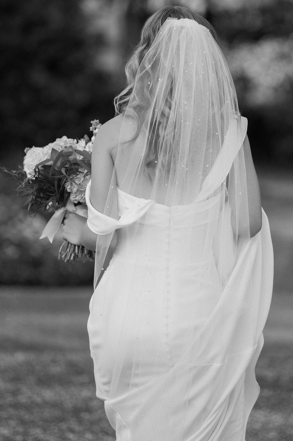 Black and white wedding photo showing flowing veil and bridal bouquet details in an artistic composition.