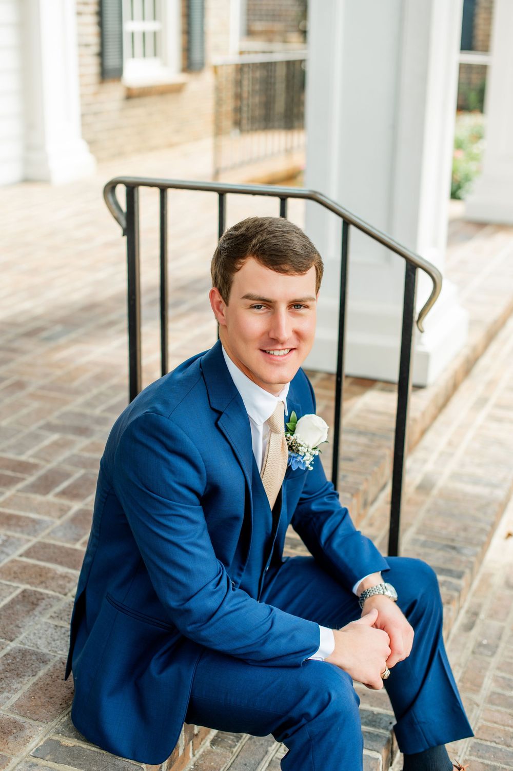 Groom in navy suit poses on brick steps during outdoor wedding portraits.