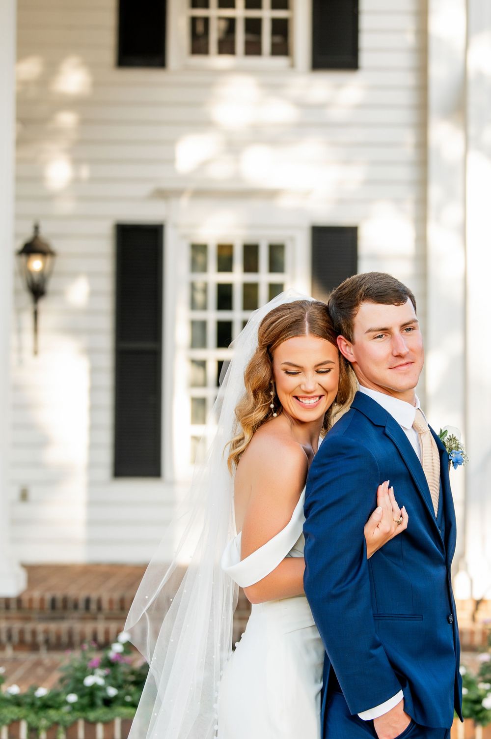 Wedding couple shares intimate moment on white columned porch of classic southern home.
