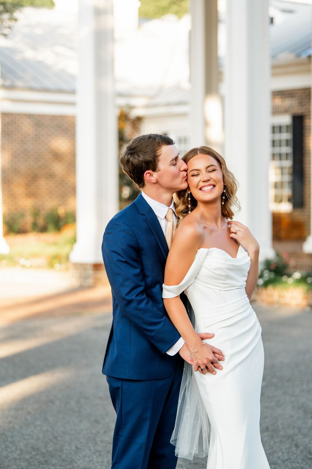 Joyful wedding couple embracing on classic southern mansion porch during golden hour.