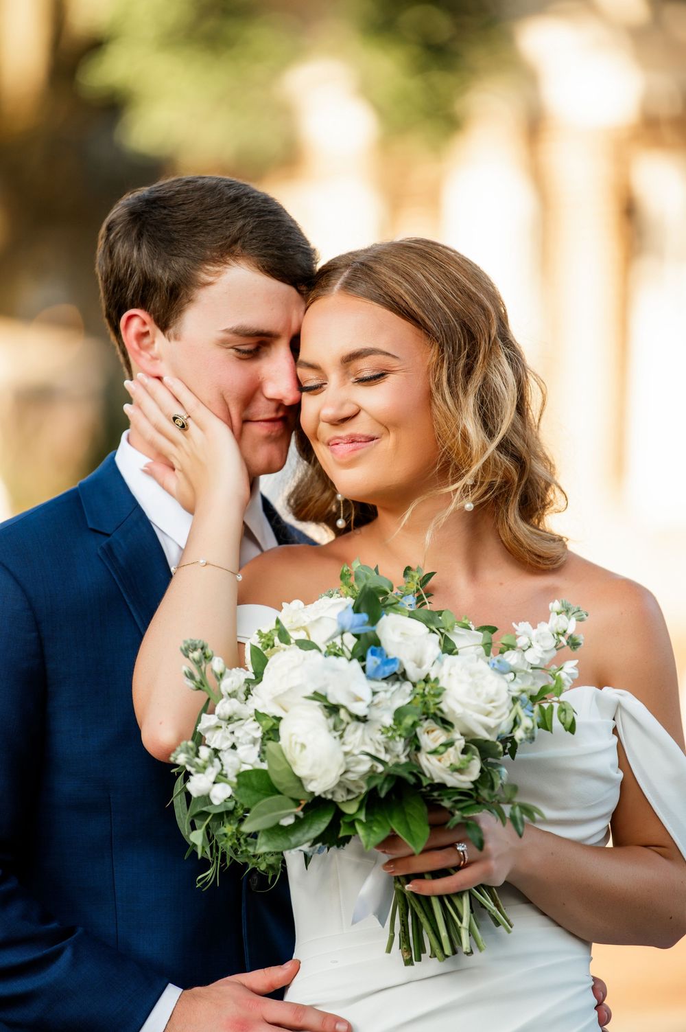 Intimate wedding portrait with white and green bouquet against architectural backdrop.