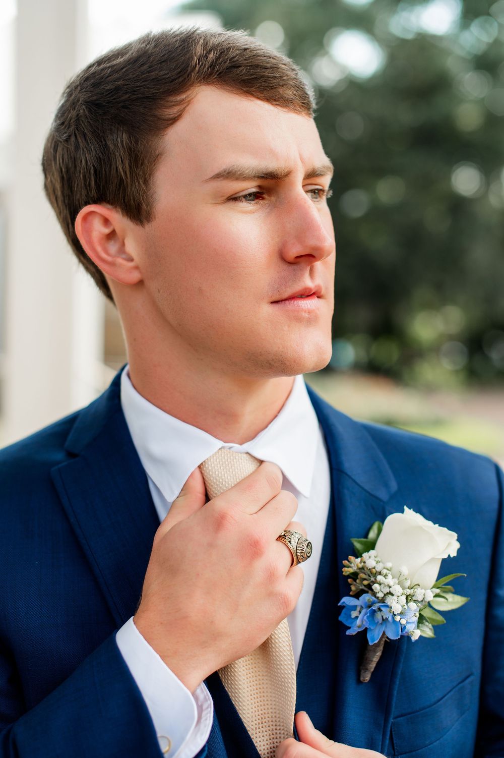 Close-up portrait series of groom in navy suit adjusting champagne tie.