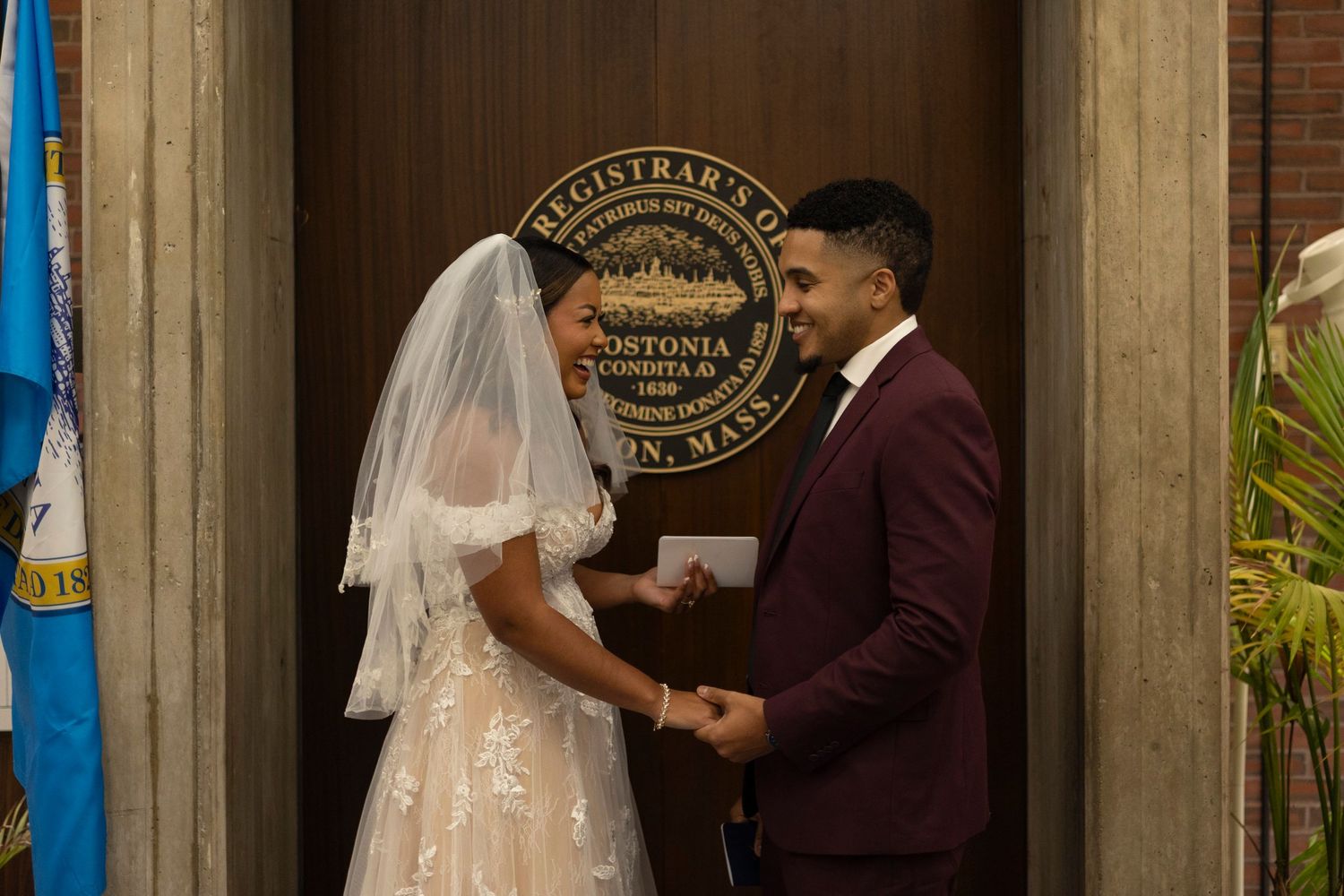 A couple exchanges vows during an elegant indoor wedding ceremony with decorative lighting and floral arrangements.