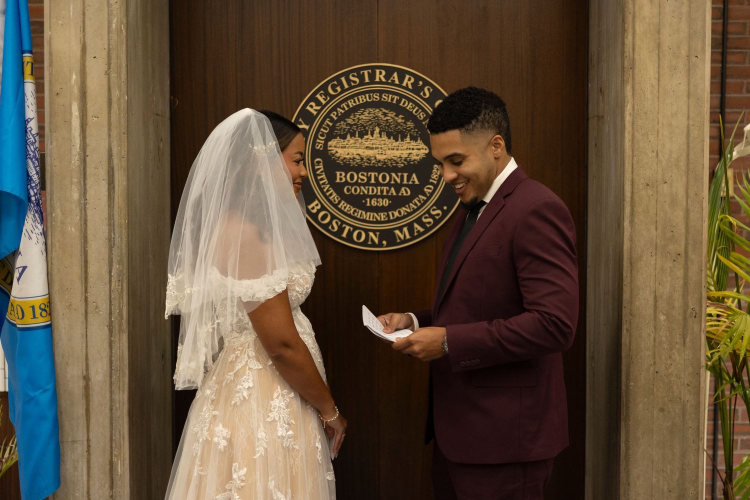A bride and groom stand together during their wedding ceremony while reading from cards or vows.