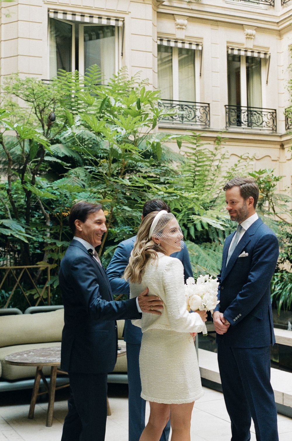 Elegant wedding ceremony in a Parisian courtyard with lush green ferns and classic architecture in the background.