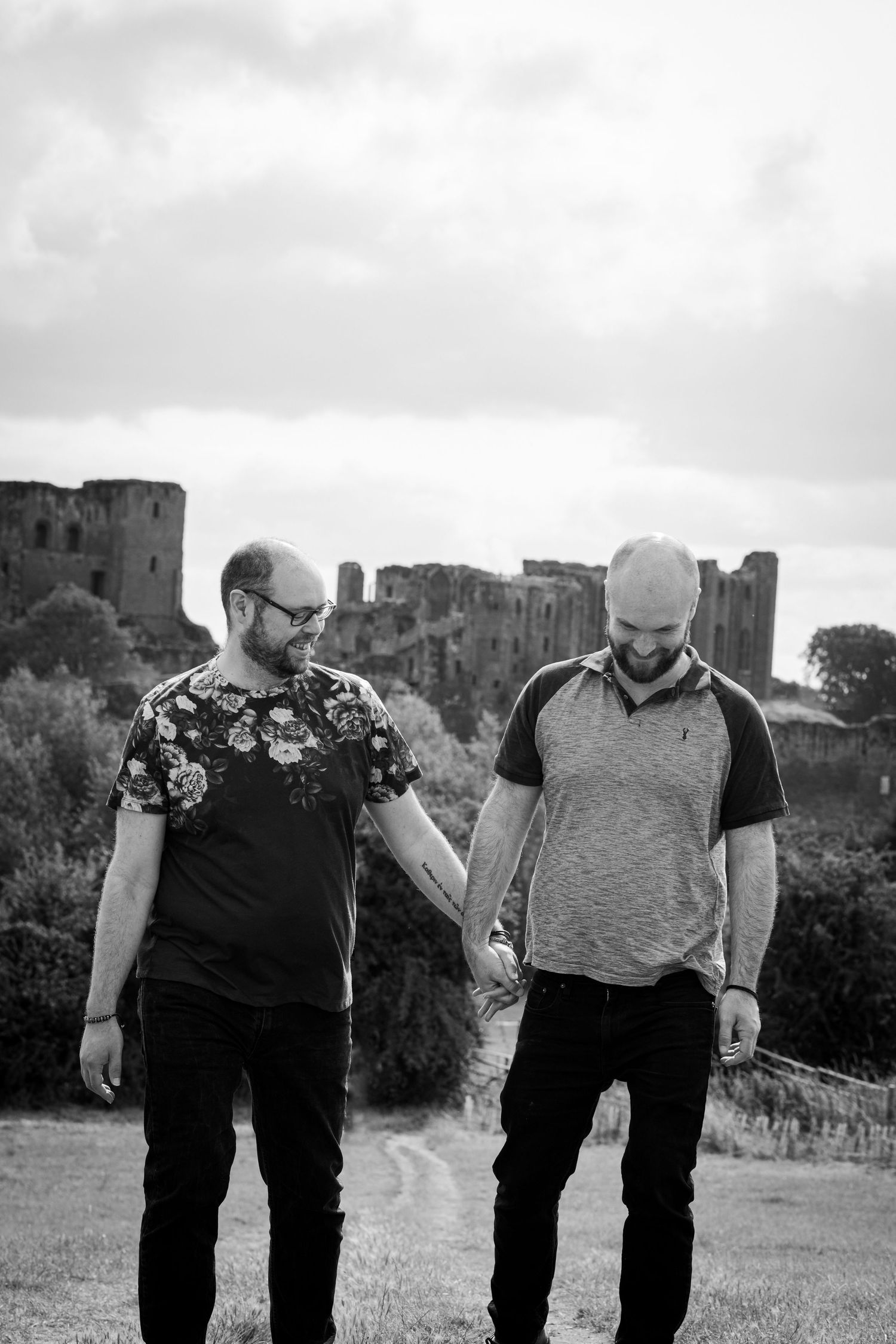 A couple holds hands while walking together outdoors wearing casual jackets in black and white photography.