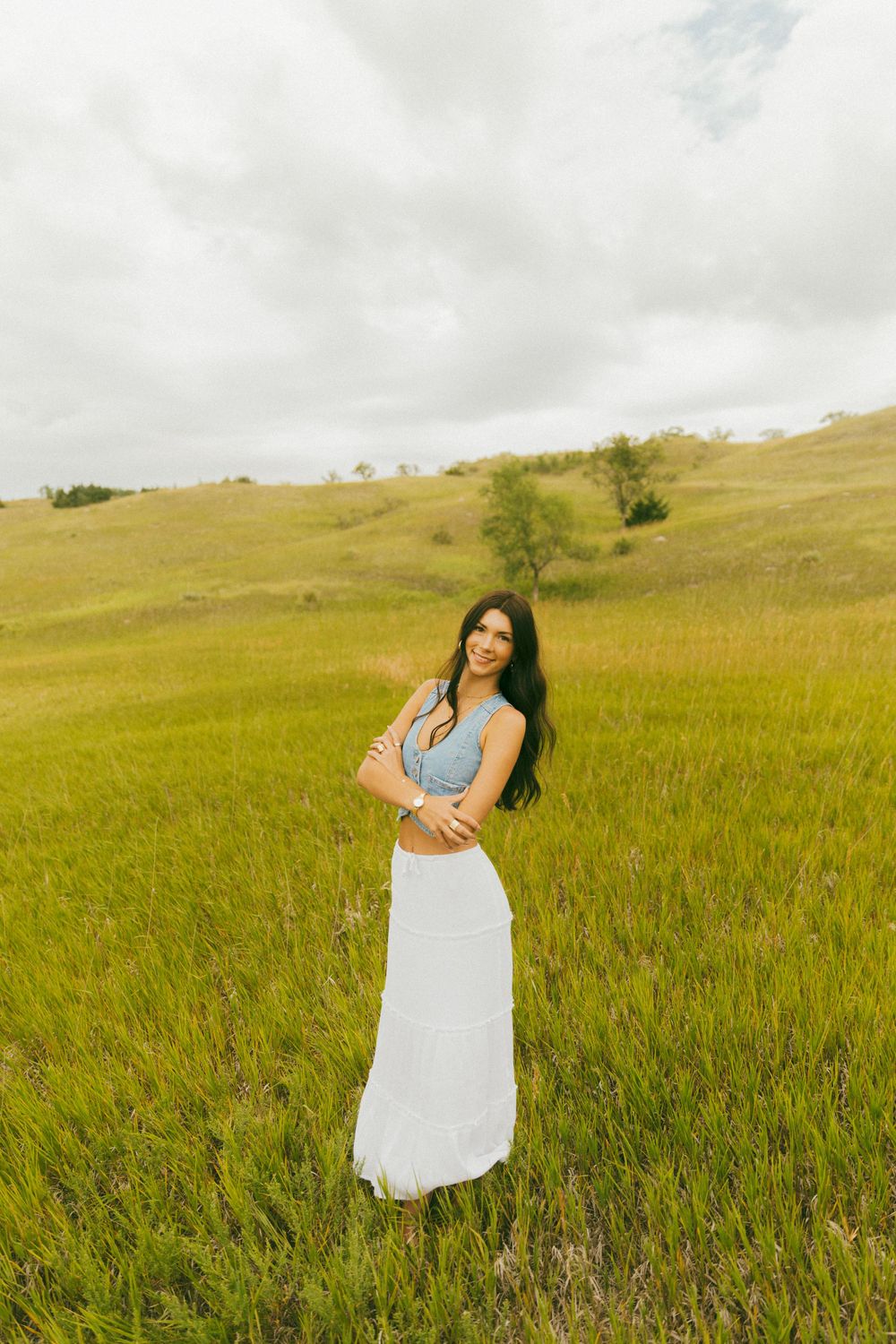 Woman in white dress twirling in a mountain meadow under cloudy skies.