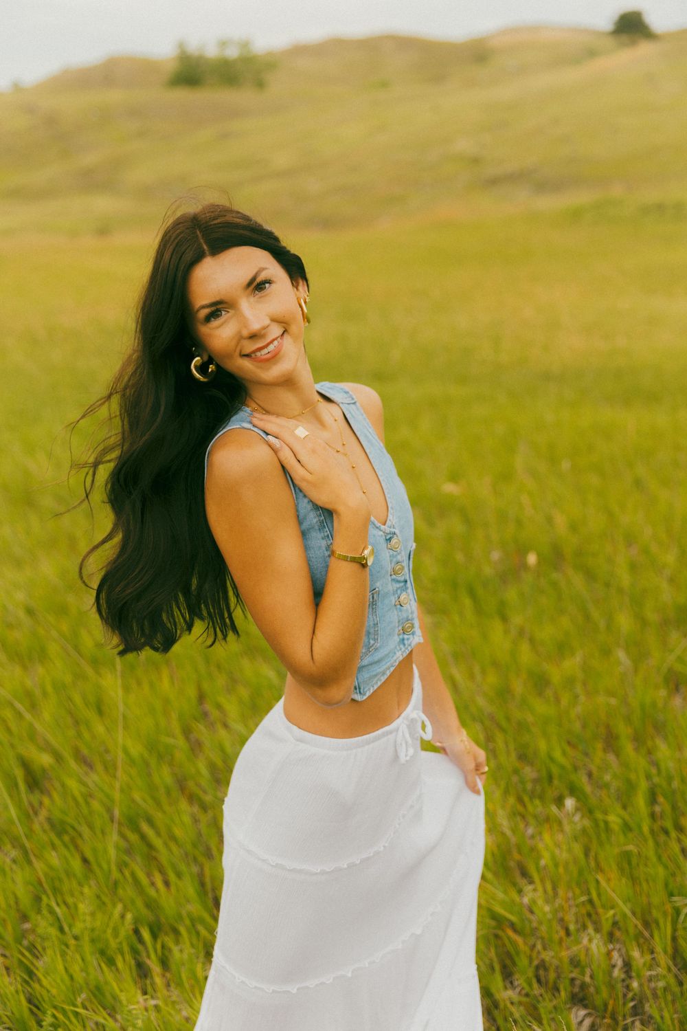 Dancing in a flowing white dress and denim top amidst tall grass in a sun-drenched field.