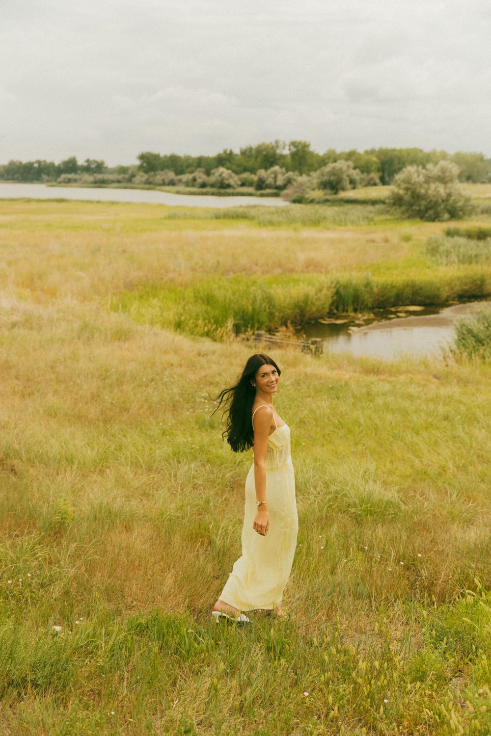 Dreamy summer photoshoot in a flowing dress near a serene pond surrounded by tall grass.