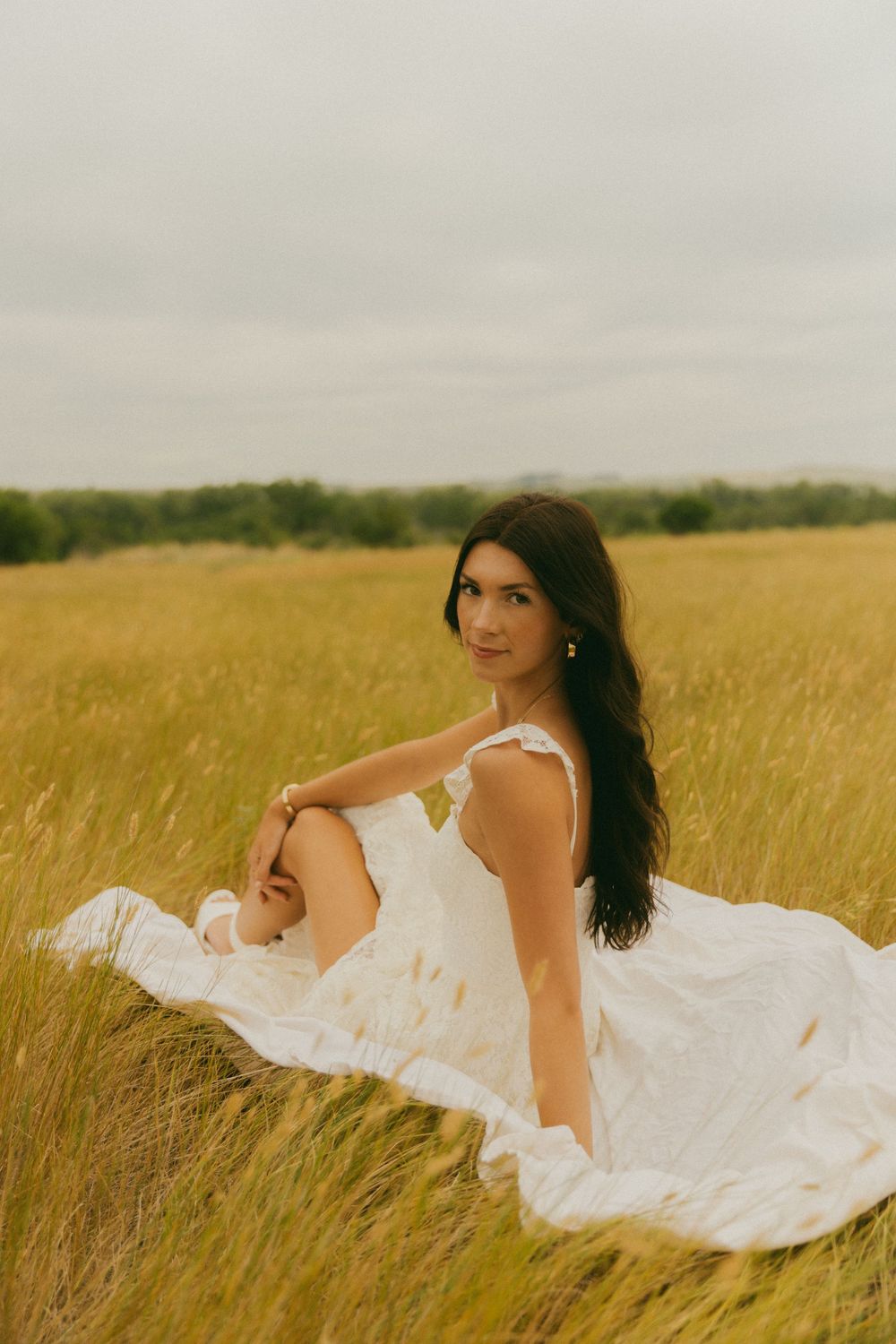 A dreamy outdoor photoshoot in a golden wheat field with a flowing white dress against a cloudy sky.