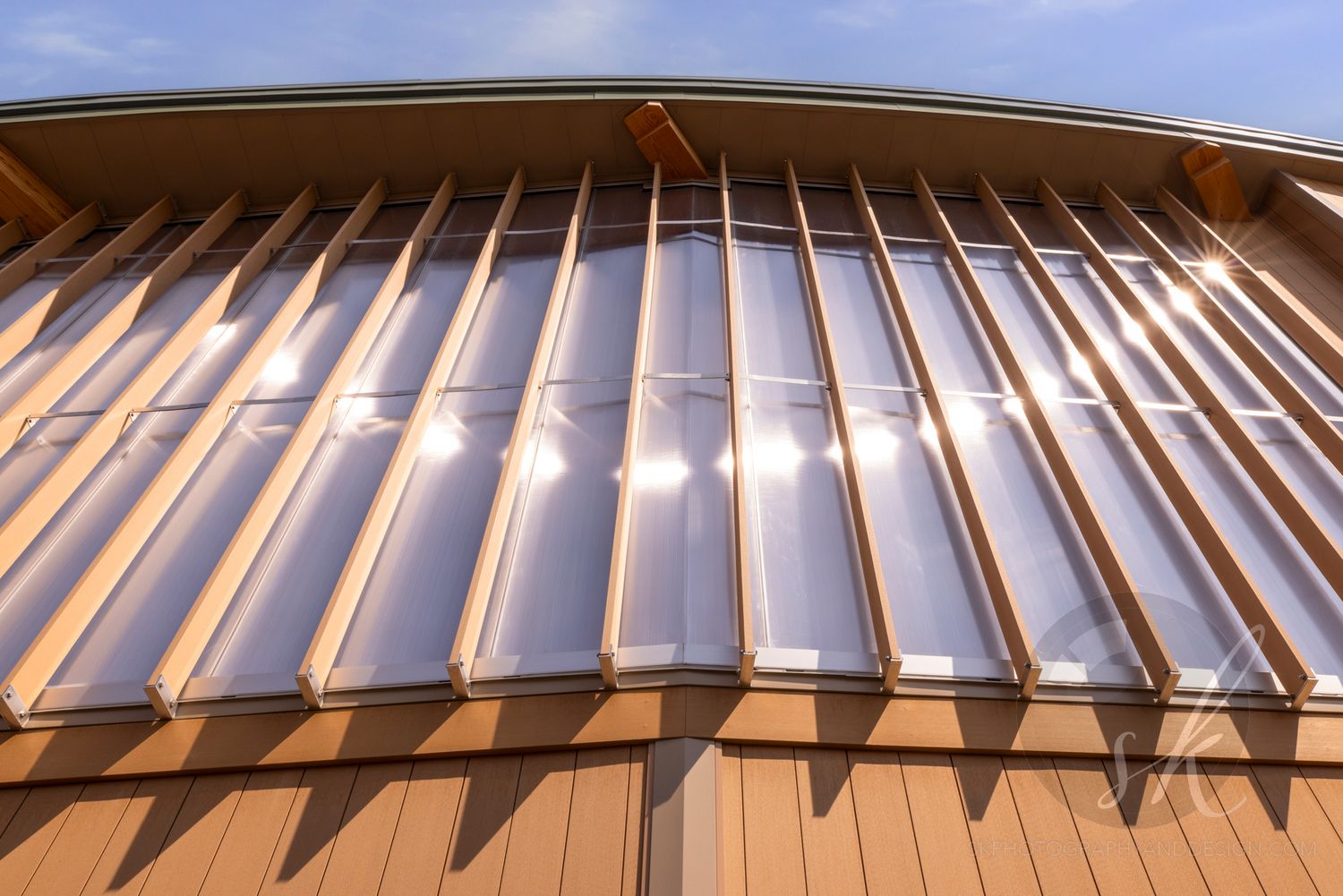 Close-up of a modern building roof featuring translucent panels between wooden beams reflecting sunlight.