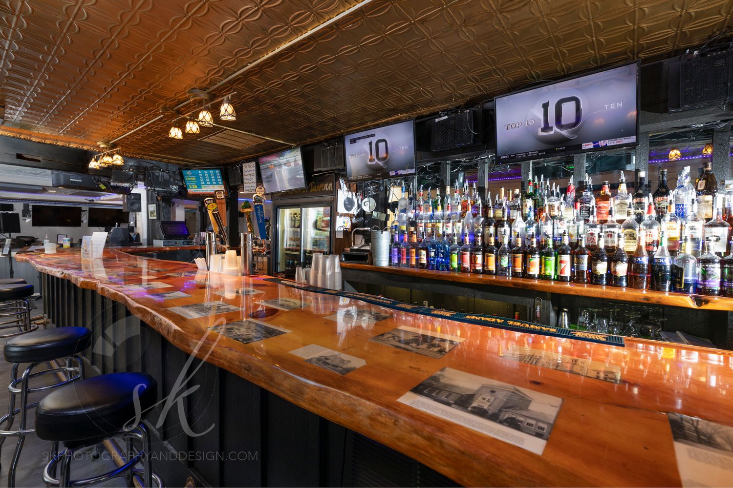 A polished wooden bar with bar stools, colorful liquor bottles, beer taps, and TVs at The Lawrence Street Tavern in Glens Falls, NY.