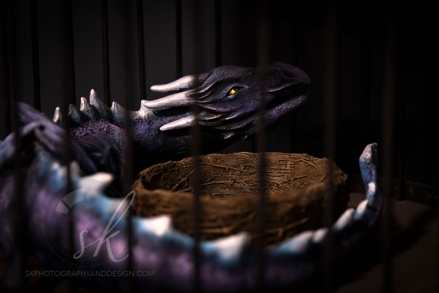 Purple dragon figurine with yellow eyes perched over a rustic woven nest bowl display piece. Saratoga Escape Rooms photo.