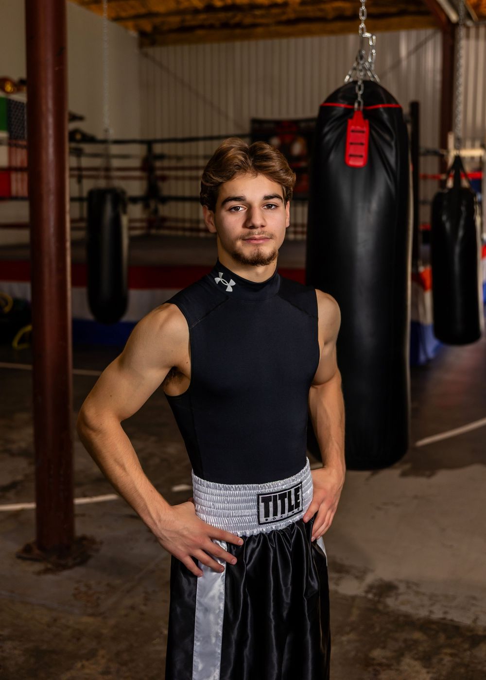 A boxer in a black tank top and grey shorts stands in a fighting stance at a boxing gym with punching bags. - senior photos in Omaha, NE