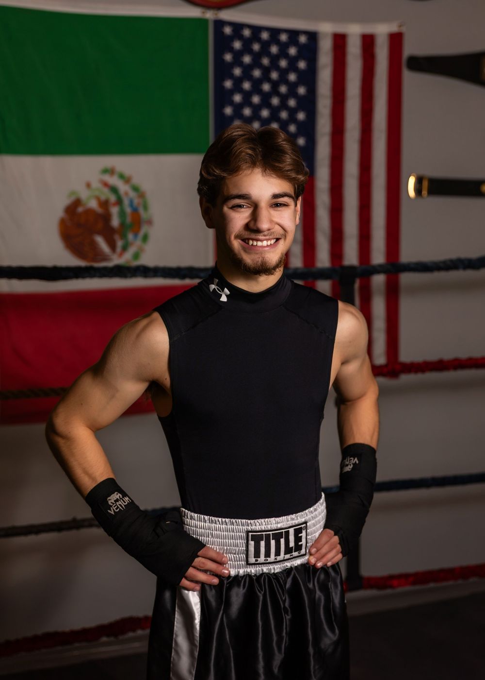 A boxer in training gear poses in front of American and Mexican flags in a boxing ring.  - senior photos in Omaha, NE
