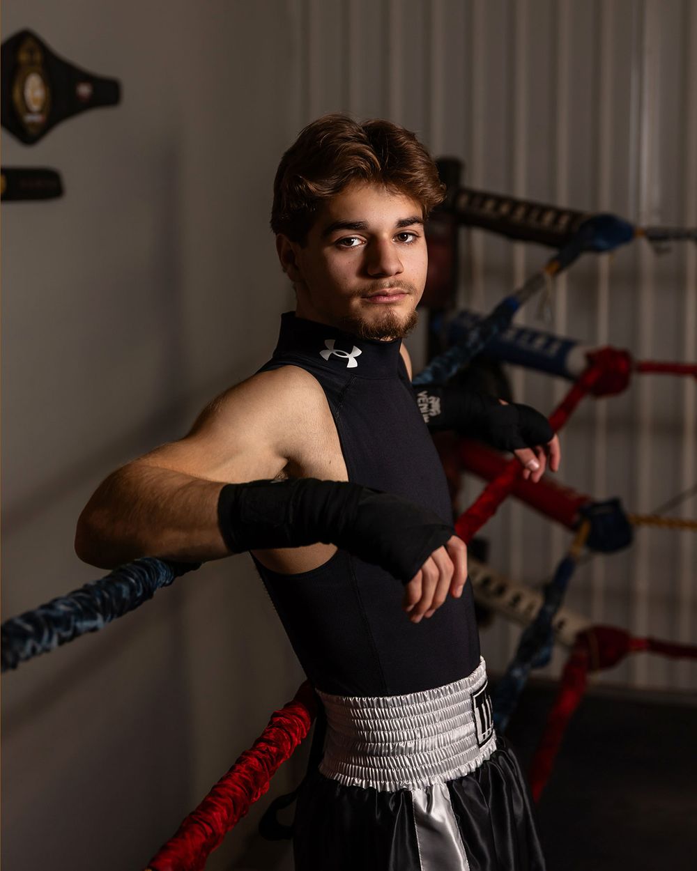 Boxing athlete practices punching techniques in dramatic lighting against flag-decorated gym wall.  - senior photos in Omaha, NE