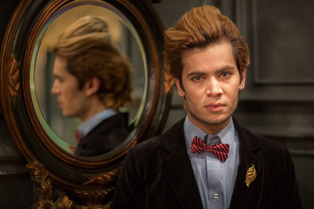 Stylish and very fashionable young man poses beside old mirror so we see his reflection too
