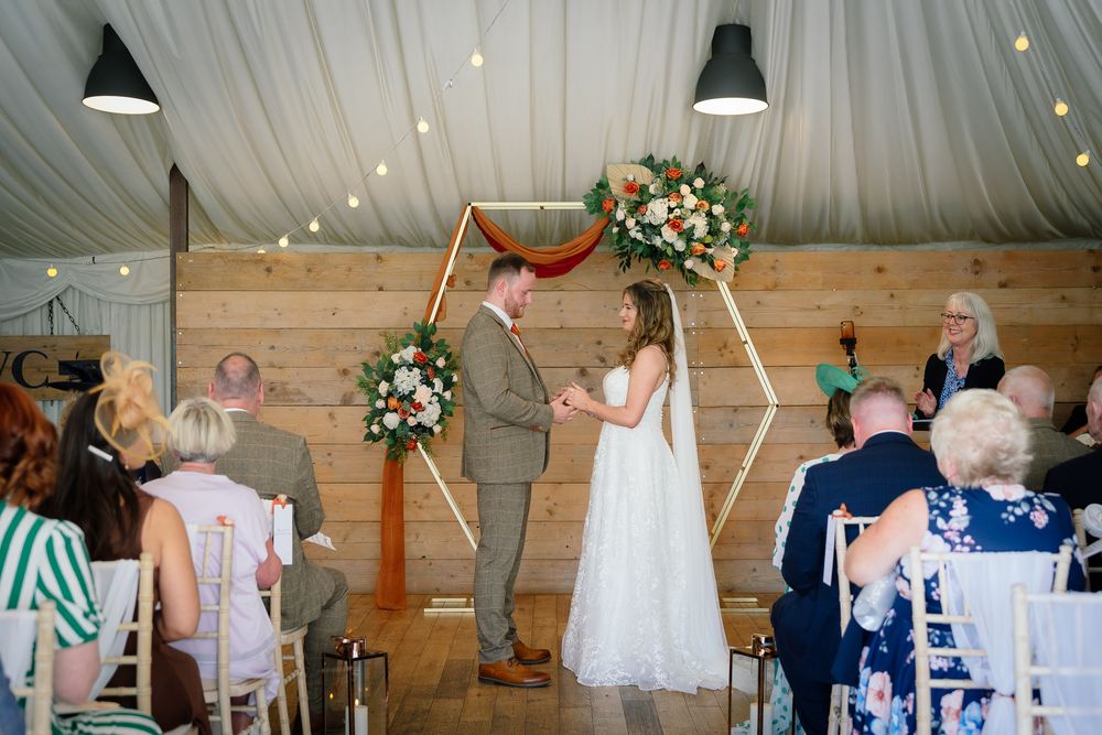 Wedding guests dance and celebrate together on a rustic wooden dance floor under string lights at an indoor reception.