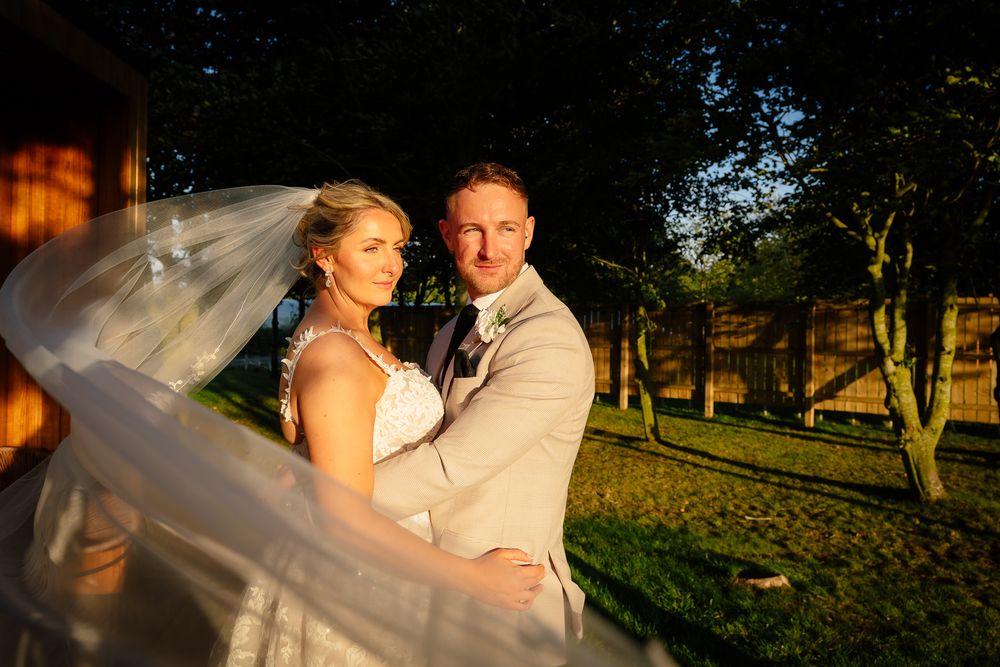 A romantic sunset wedding portrait shows a couple embracing as the bride's veil flows dramatically in the golden light.