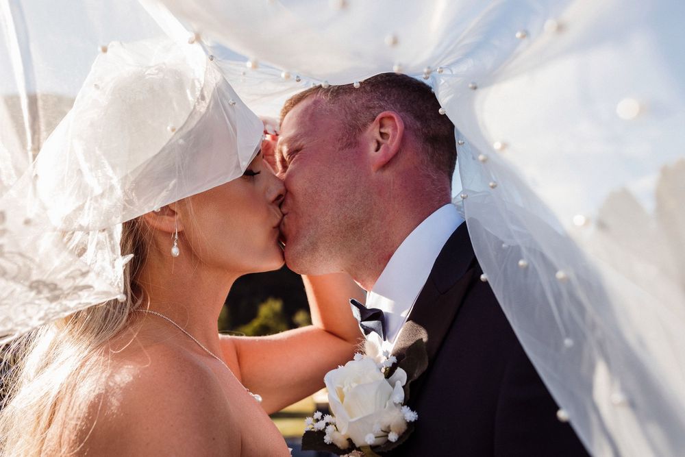 A romantic couple shares a tender kiss under a white veil during their wedding celebration.