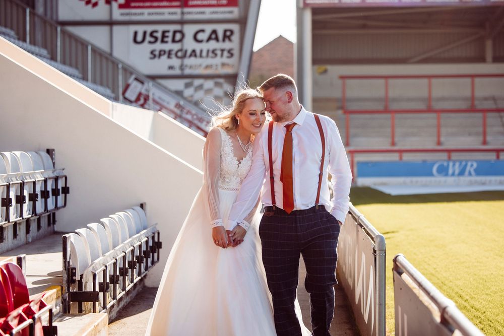 A couple in wedding attire poses on a staircase with red and white decor in the background.