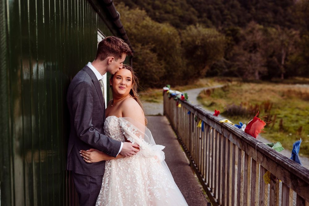 A romantic wedding couple shares intimate moments on a rustic wooden bridge in a natural outdoor setting.