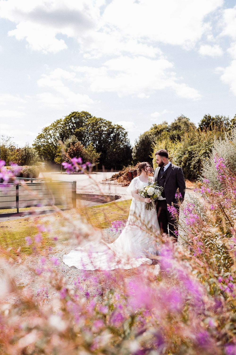 A couple shares a romantic moment in a garden filled with blooming purple wildflowers on a sunny summer day.