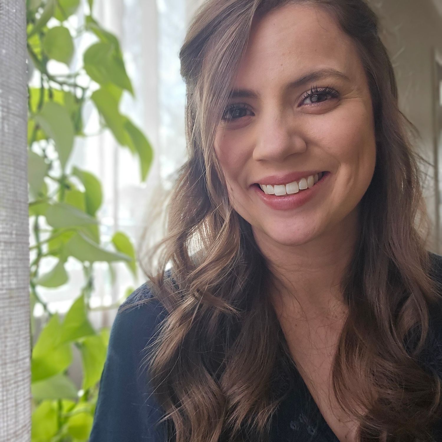 Woman smiling next to indoor plant.