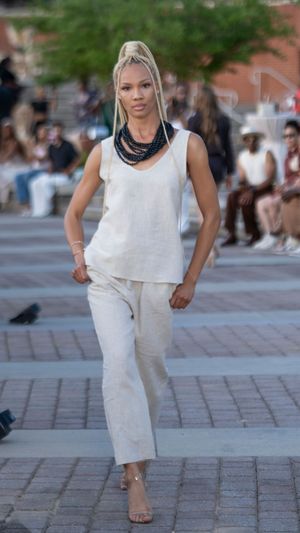 Fashion model walks runway in all-white ensemble featuring loose-fitting pants and sleeveless top.