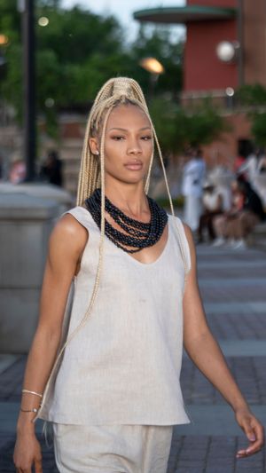 A model in a white sleeveless top walks confidently down an outdoor runway.