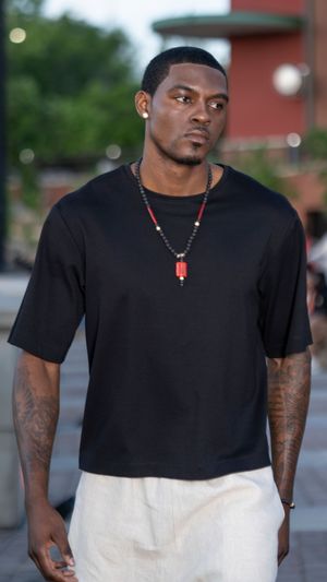 Street fashion look featuring black t-shirt and white pants on brick paved walkway.