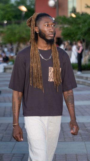 Model showcases casual streetwear look with black tee and white pants on outdoor runway.