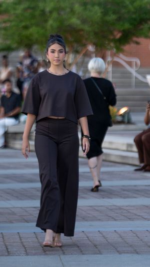 A model showcases an all-black ensemble featuring a cropped top and wide-leg pants on an outdoor catwalk.