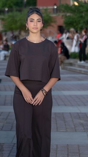 Model presents all-black ensemble with short sleeves on stone paved runway.