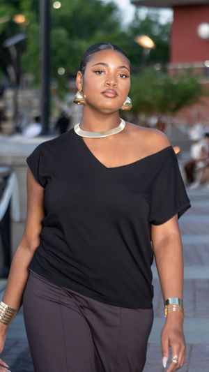Model wearing asymmetrical black top poses on outdoor runway.