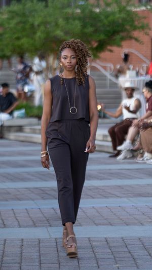 Model showcases sleek black sleeveless jumpsuit on outdoor runway.