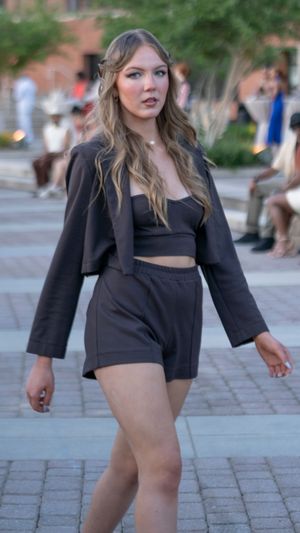 A person in a black crop top and matching shorts walks on a brick pathway in an urban setting.