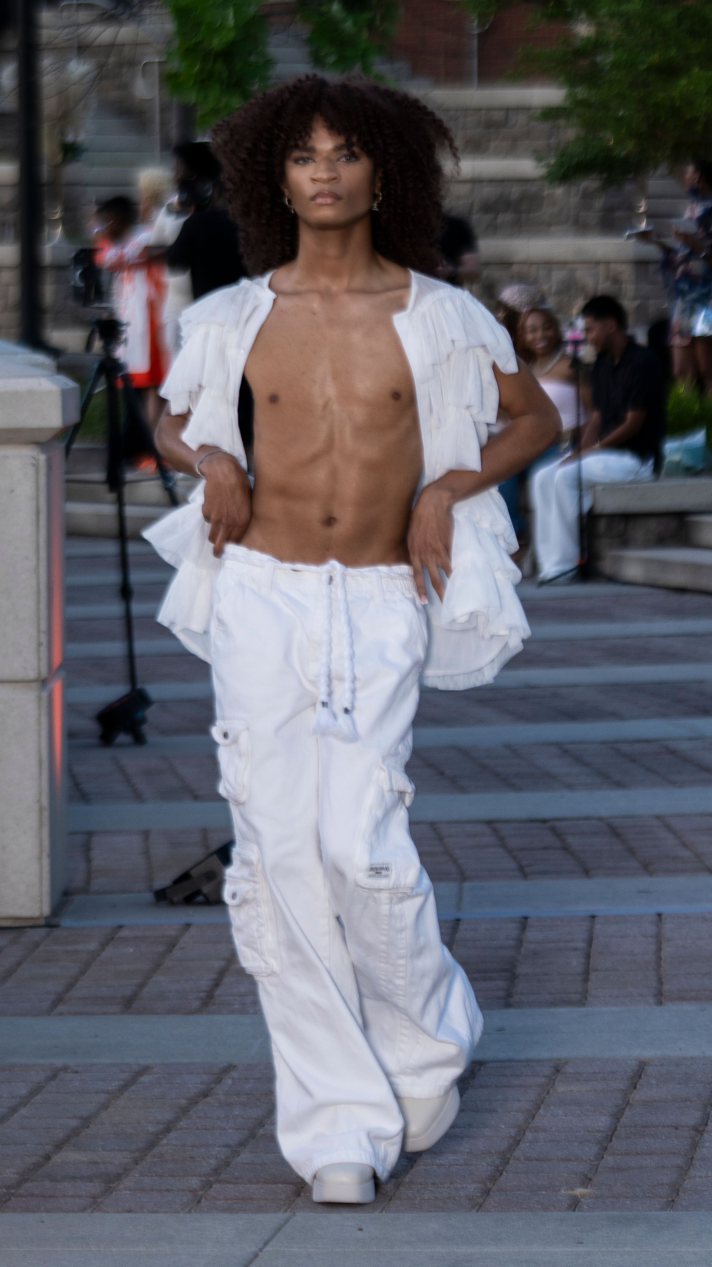 Model presents all-white ruffled ensemble with cropped top on outdoor runway.