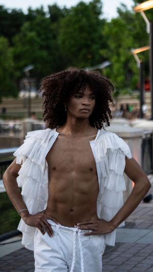 Model in white ruffled shirt performs dramatic pose during outdoor fashion show.