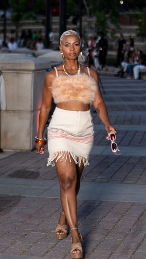A model struts in a cream-colored fringe dress with feather details during an outdoor fashion show.